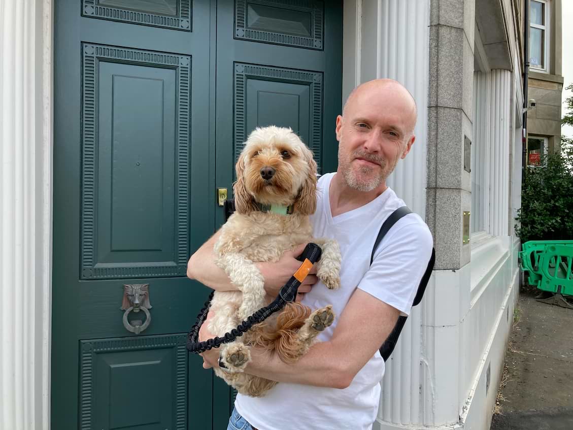Ben holding a cavapoo dog in front of a green door